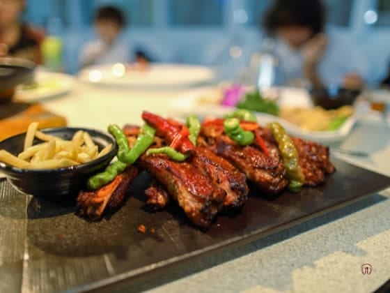 Żeberka w glazurze barbecue z warzywami i frytkami na czarnym półmisku.