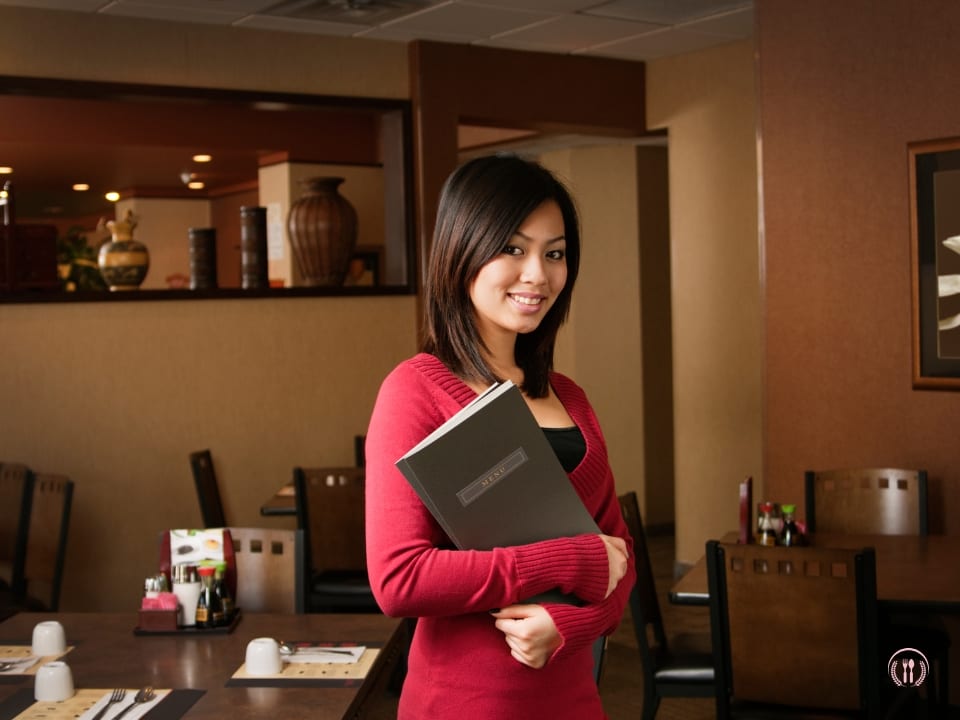 Maitre d’ Amelia Ryś uśmiecha się, witając gości w eleganckim foyer restauracji.