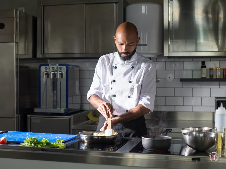 Sous-chef Maks Wroński przy stanowisku kuchennym z zestawem przypraw i naczyniami ze stali nierdzewnej.
