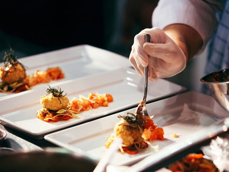 Szef kuchni nakłada porcję dania na biały talerz w trakcie serwisu.
