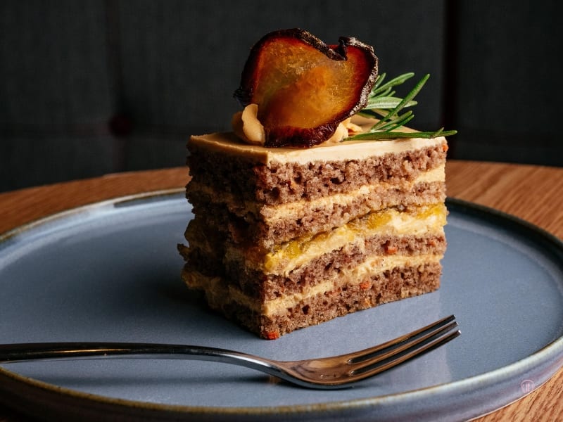 Warstwowe ciasto z kremem i karmelizowaną gruszką na talerzu w ciemnym tle.