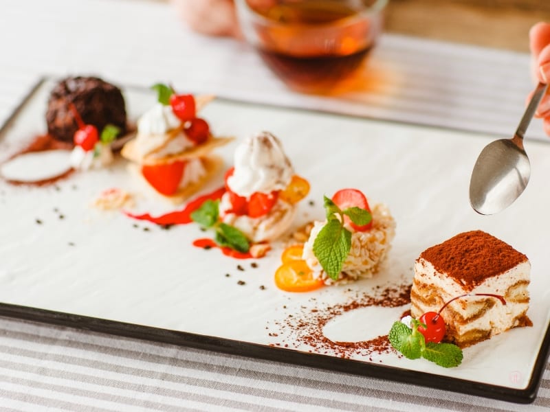 Talerz z różnymi porcjami deserów ozdobionych owocami i kremem.