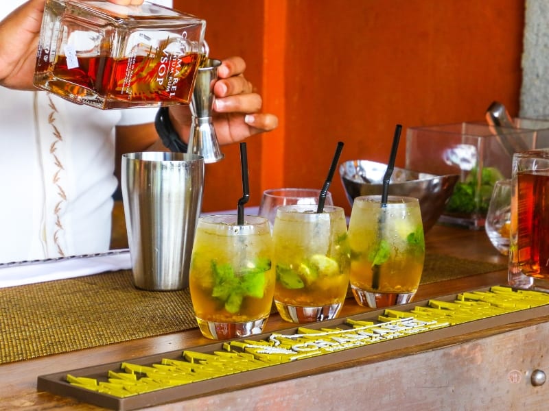 Barman nalewa rum do szklanek z miętą i lodem podczas przygotowywania koktajlu.