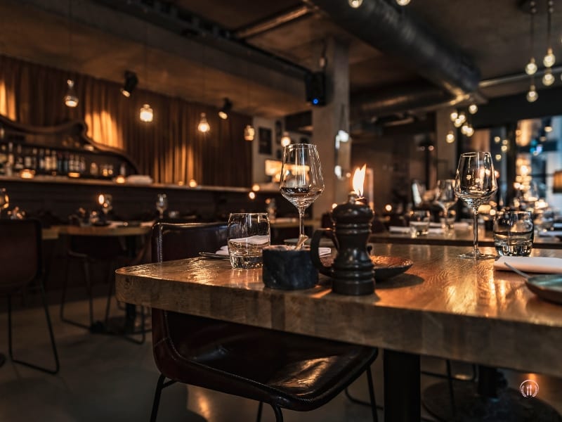 Przyciemniona sala kolacyjna z mosiężnymi lampami i eleganckimi nakryciami stołów.