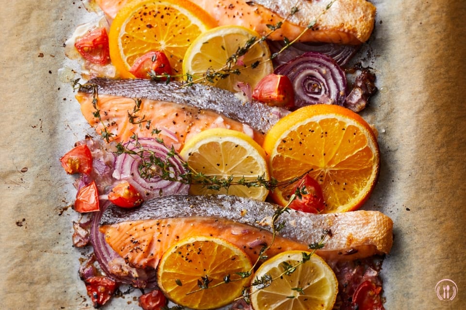 Filet dorsza pieczony z plastrami cytrusów, czerwoną cebulą i pomidorkami na papierze do pieczenia.