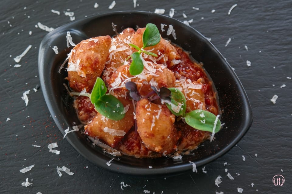 Małe kluseczki w sosie pomidorowym, posypane parmezanem i listkami bazylii w czarnej misce.