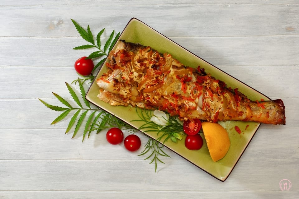 Porcja sandacza z rumianą skórką na prostokątnym talerzu, z pomidorkami i cząstką cytryny.